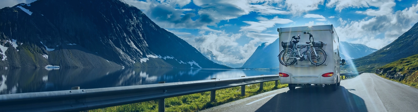 Camping-car roulant au bord d’un lac de montagne sous un ciel bleu, symbolisant liberté, évasion et confort de voyage.