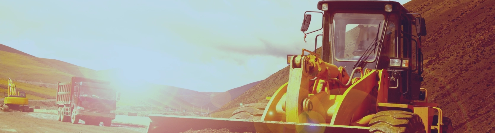 Engins de chantier en pleine activité dans une zone montagneuse, sous un fort soleil, illustrant puissance, robustesse et productivité sur le terrain.