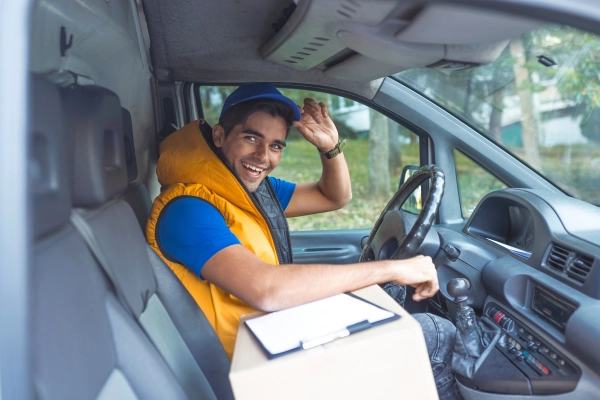 Livreur souriant au volant de son utilitaire, prêt pour une tournée, illustrant la fiabilité et la bonne humeur des professionnels de la route.