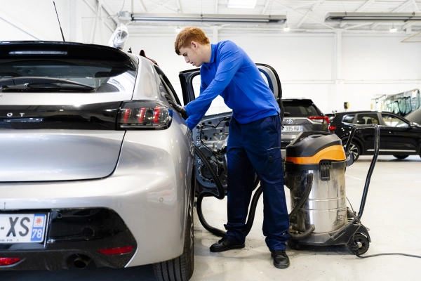 Technicien Mondial Pare-Brise nettoyant l'intérieur d'une voiture à la suite d'une opération dans l'atelier