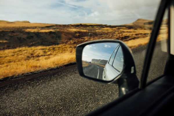 Vue du paysage à travers le rétroviseur d’un véhicule en mouvement sur une route de campagne. Une invitation à prendre la route l’esprit tranquille, avec un vitrage en parfait état.