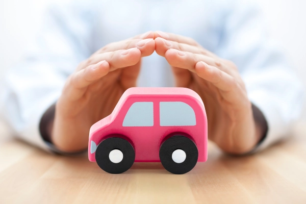 Mains protectrices entourant une voiture miniature rose, représentant la sécurité et la tranquillité offertes par une assurance auto.