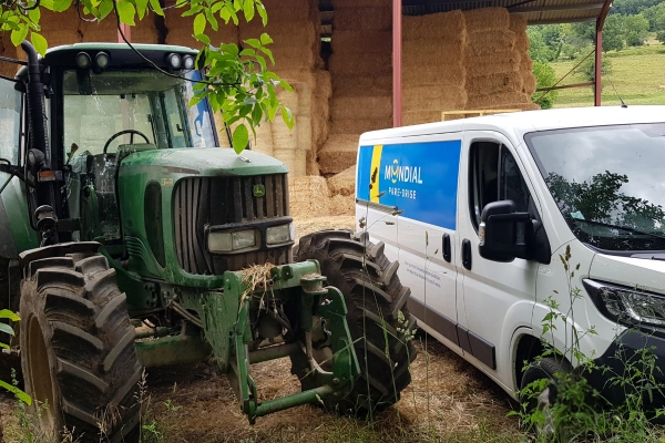 Véhicule d’intervention Mondial Pare-Brise garé à côté d’un tracteur agricole dans une ferme, illustrant le service de proximité même en zone rurale.
