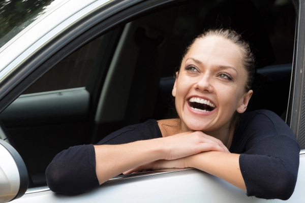 Conductrice souriante à la fenêtre de sa voiture, exprimant la sérénité et la satisfaction après une intervention réussie.