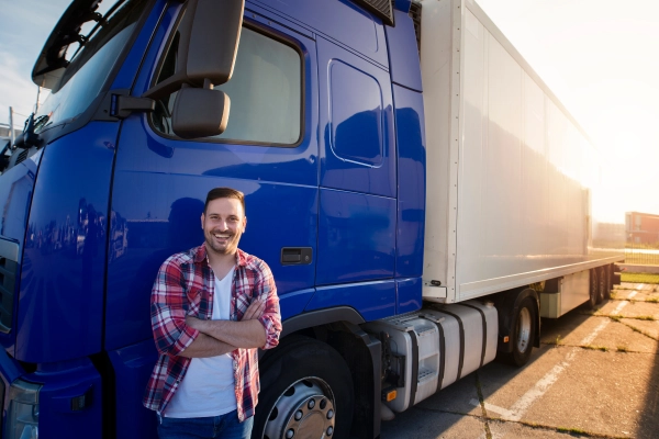 Chauffeur routier souriant devant son poids lourd bleu au coucher du soleil – la sérénité d’un professionnel confiant, grâce à un vitrage parfaitement pris en charge.